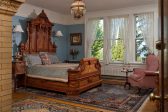 Ornate wood bed with side table, pink chair, and three windows