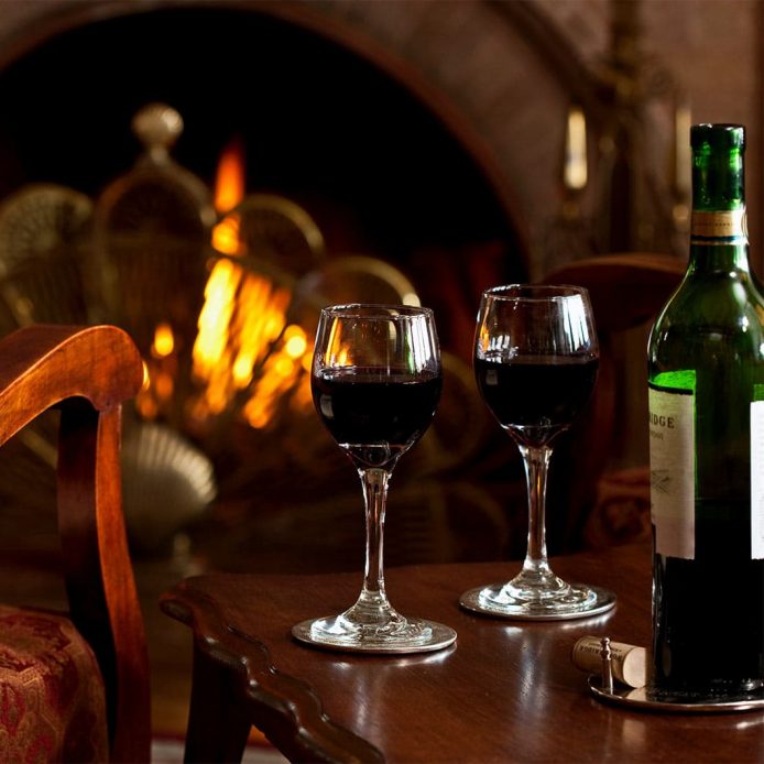 Bottle or red wine with two glasses in front of fireplace