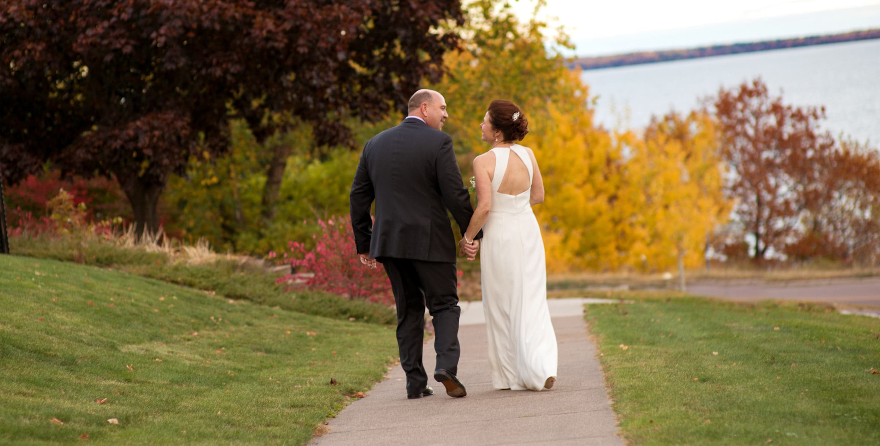 Bride and Groom walking down the sidewalk with lake in background