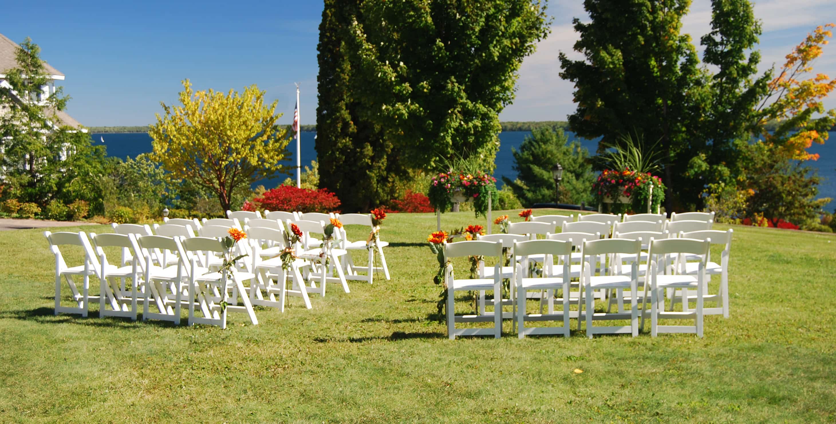 Lawn set up for ceremony with white chairs and water in the background