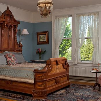 Ornate wood bed with side table, and windows