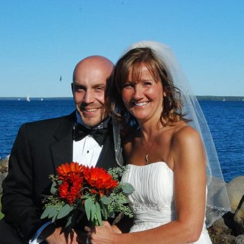 Happy bride and groom by the water with red bouquet