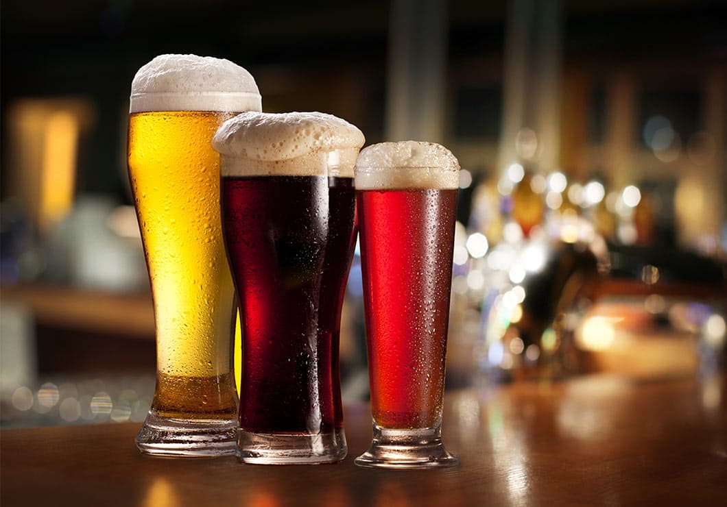 Three pilsner beer glasses of various colors