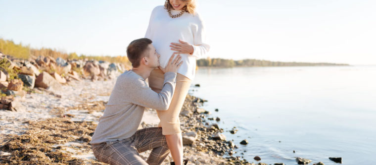 A soon-to-be-father kisses his partner's belly on Lake Superior's shores during their babymoon in Bayfield, WI.